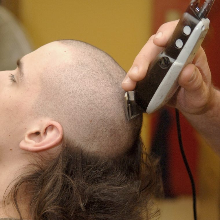 A barber runs electric clippers up the side of a client's head.