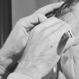 Shop detail: two hands hold a comb against a client's hair in a black-and-white photograph.
