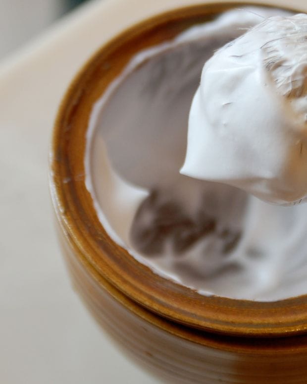 A shaving brush resting in a wooden bowl of thick white lather.