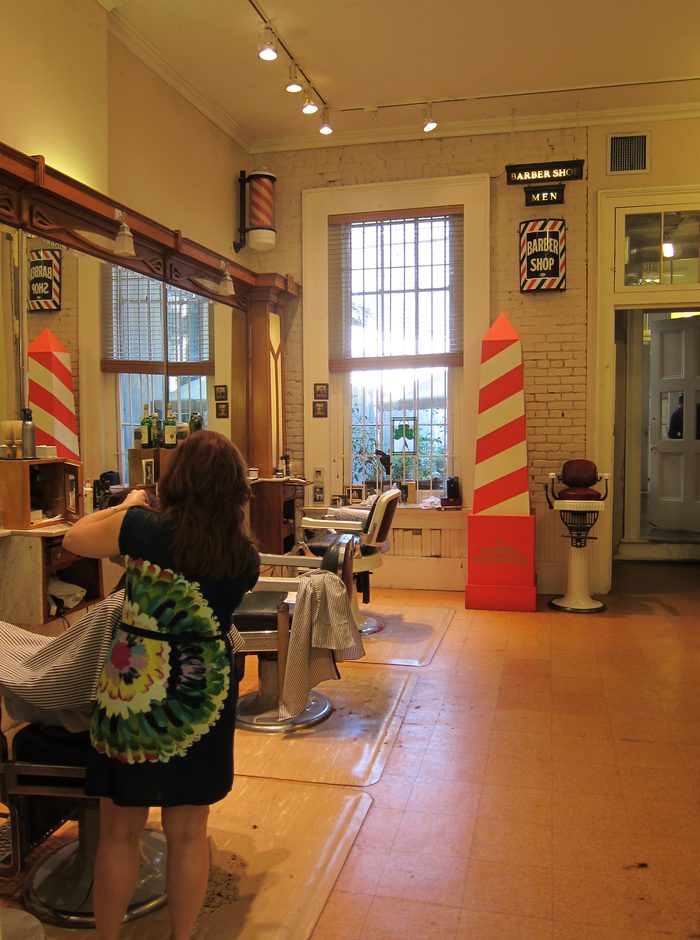 A barber shop interior with tall mirrors, striped poles and a barber at work