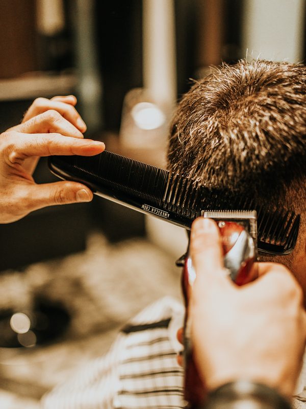 A barber blending the back of a client&rsquo;s neck with comb and clipper