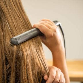 A flat iron drawn down a length of long, straight brown hair.
