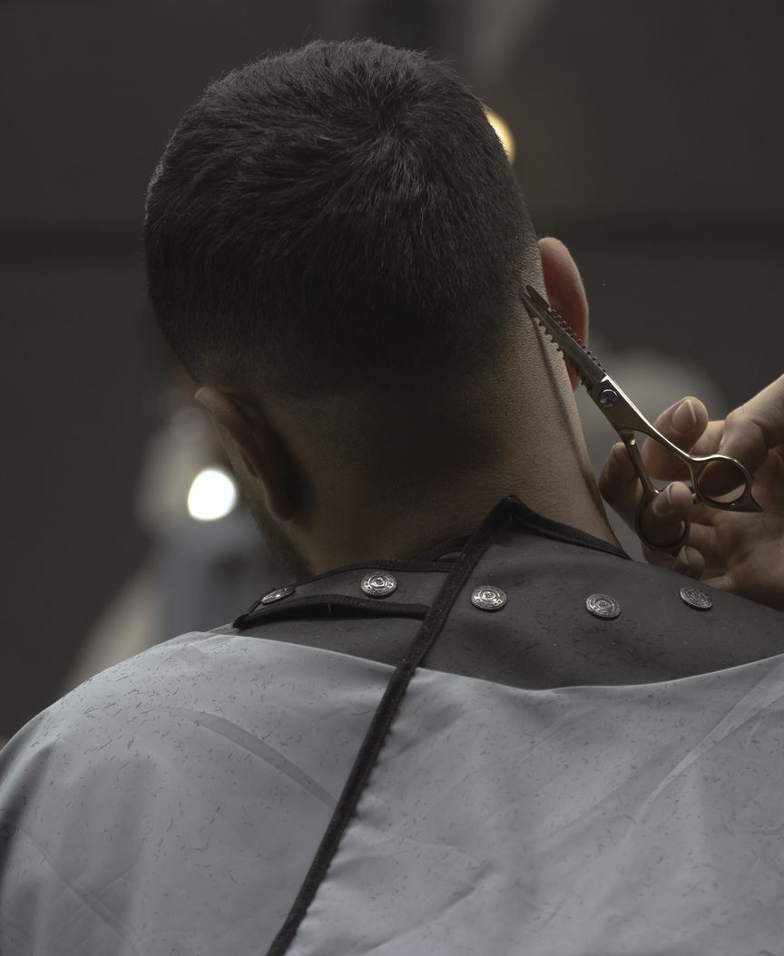 Shears working at the nape of a caped client's head. Photographed from behind; no face is in frame.