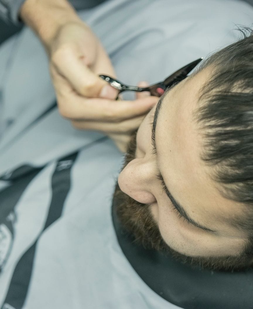 Close view of shears taking a line along a caped client's hairline.