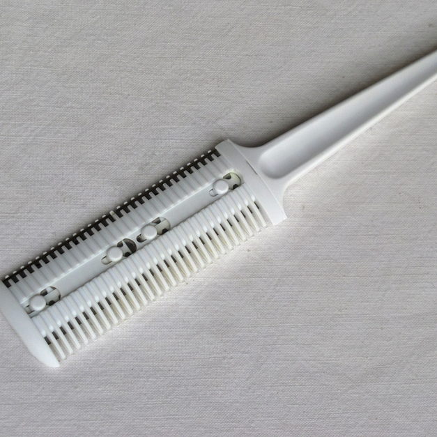 A clean white razor comb resting on a folded pale woven cloth.