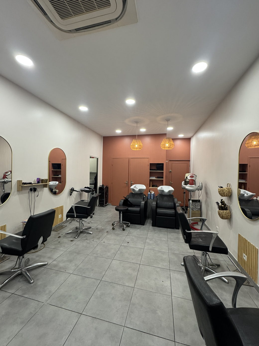 A compact salon room with two backwash basins, arched mirrors and black chairs on tiled floor.