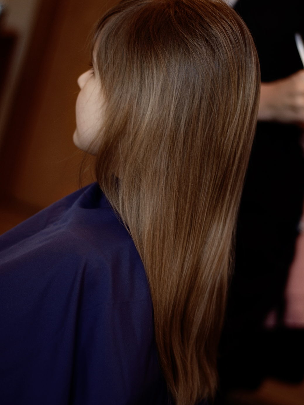 Long straight brown hair falling over a blue cape, seen from behind with the face out of frame.