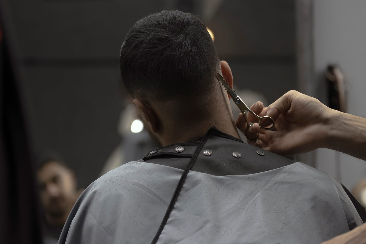 A close cut being finished at the nape with scissors, the client seen from behind.