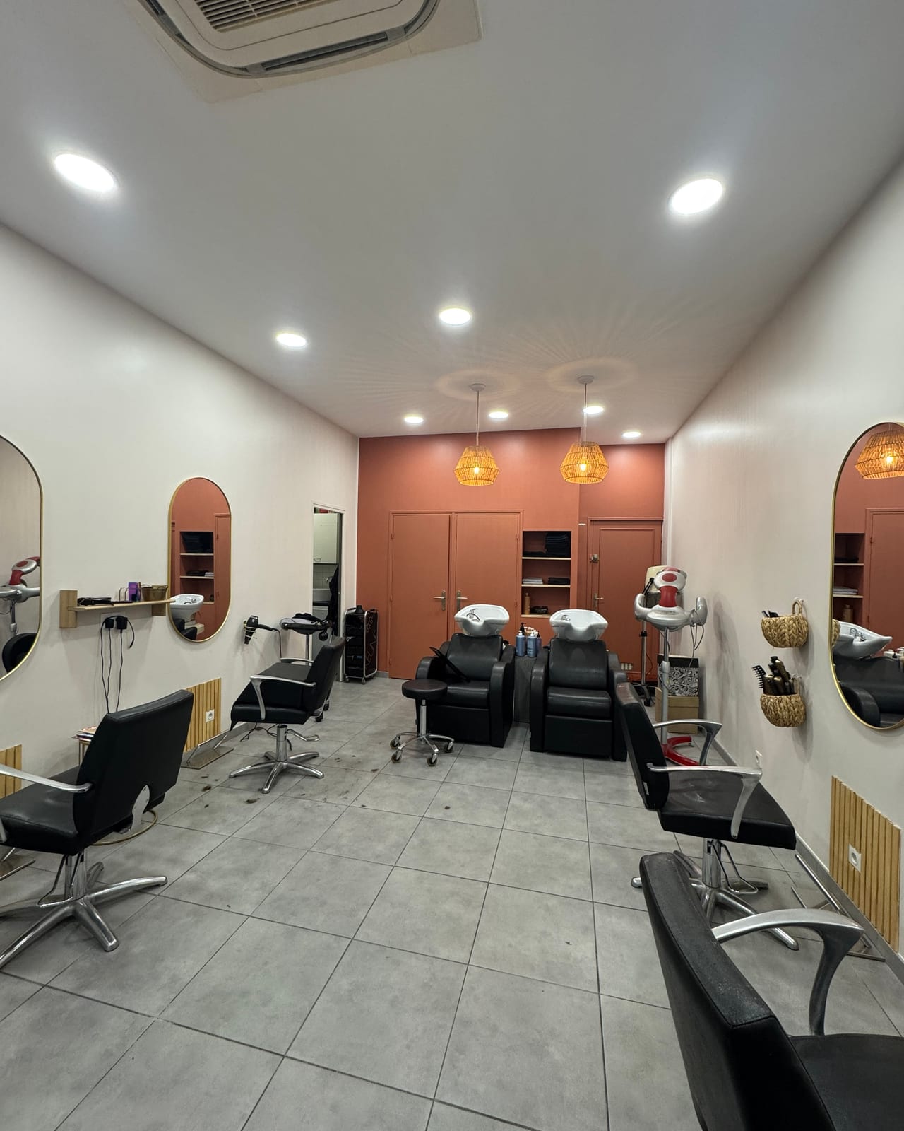 Two wash chairs and arched mirrors against a terracotta wall in a salon.
