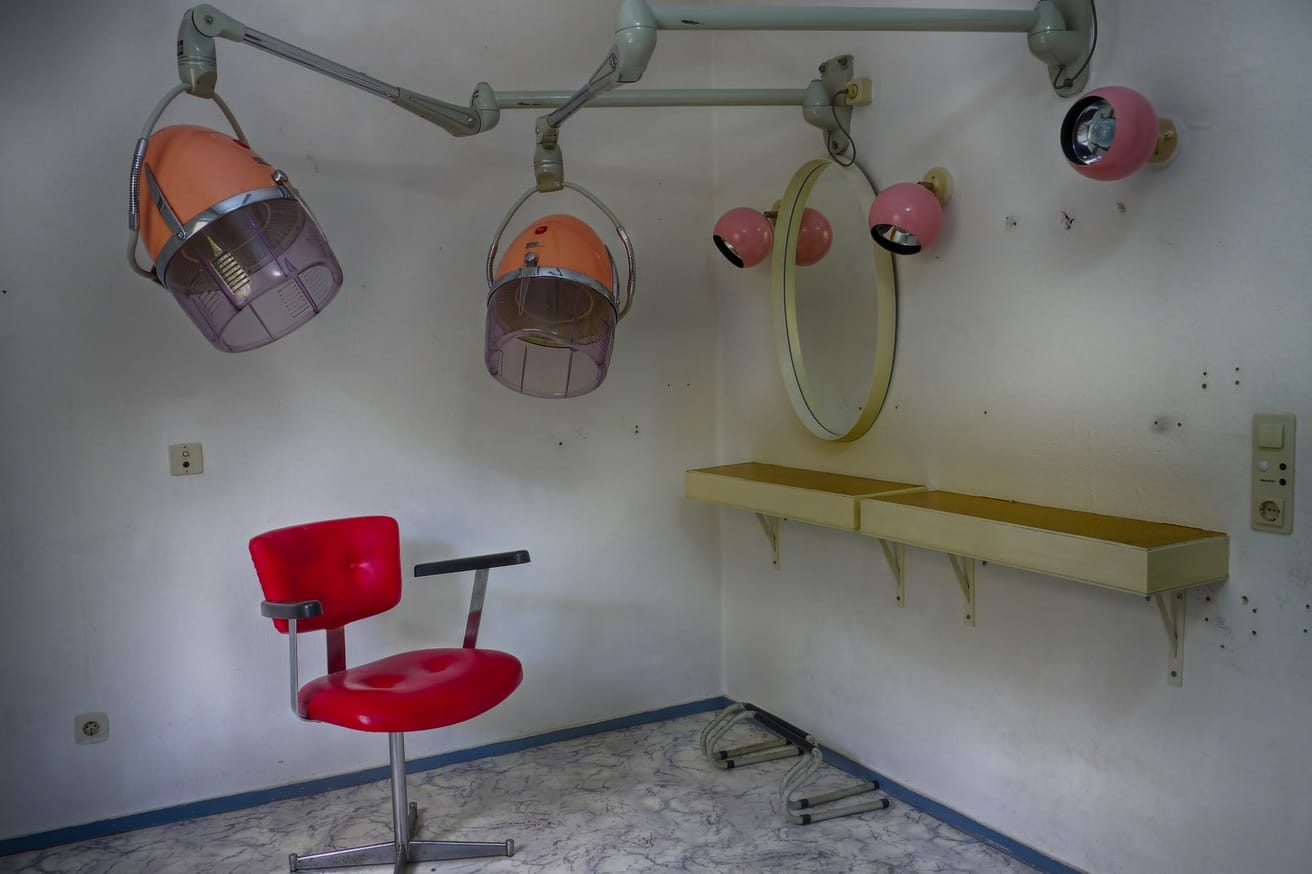A 1970s salon with a red styling chair and a row of hood dryers.