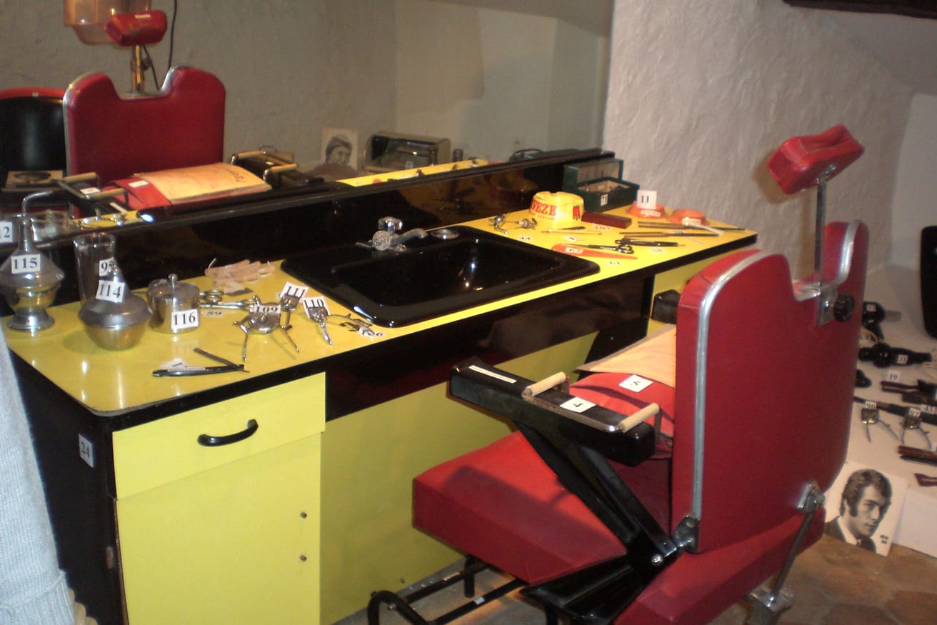 A vintage styling station painted yellow, with a red chair in front of the mirror.