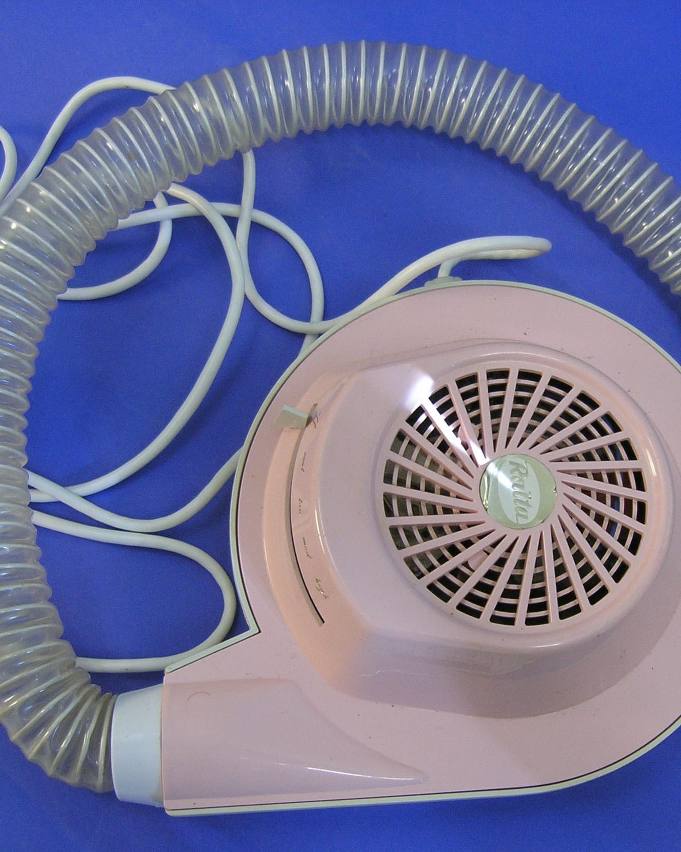A pink hand-held salon hair dryer with its coiled hose, photographed on a blue backdrop.