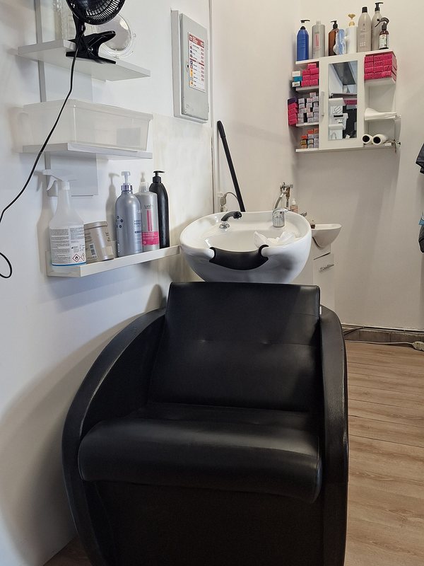 A white backwash basin and reclining chair beside a shelf of treatment bottles