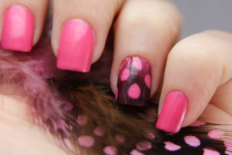 Fingernails painted pale peach with a fine feather design drawn across each one.