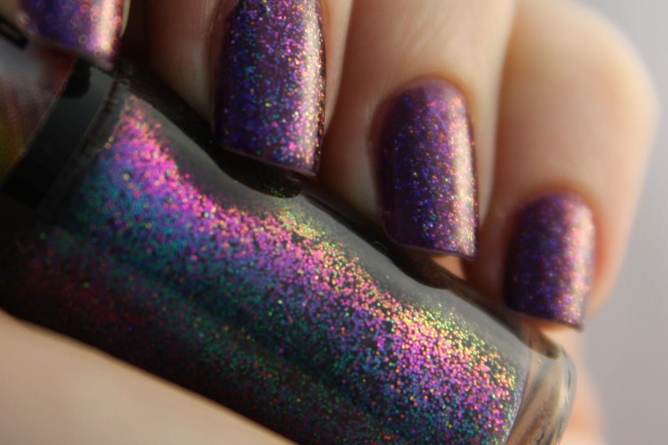 Nails in a purple glitter polish beside the bottle, which shifts from pink to green in the light.