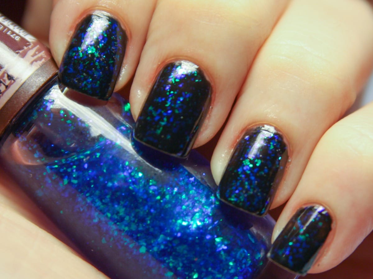 Nails painted in dark blue glitter polish, held against a bottle of the same polish.