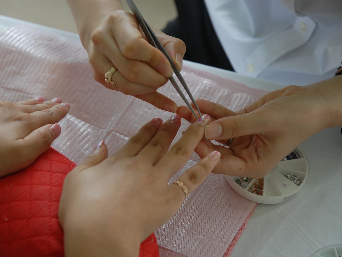 A nail technician shaping a client's nails with a fine tool at a manicure table.
