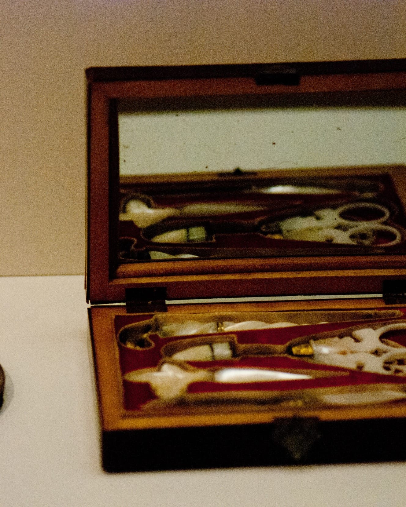An antique manicure set in an open wooden case lined with red fabric.