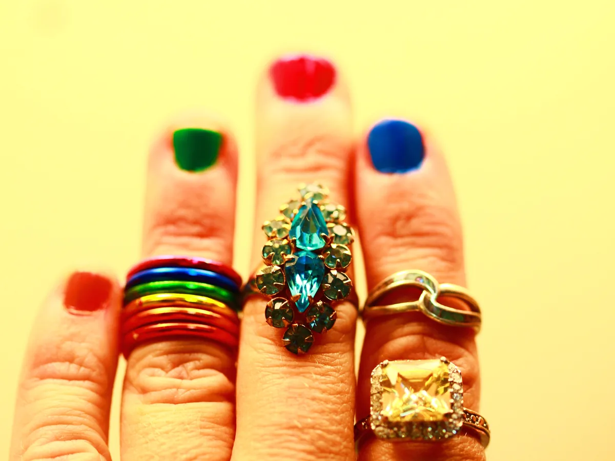 Fingers with red, green and blue nails against a yellow ground
