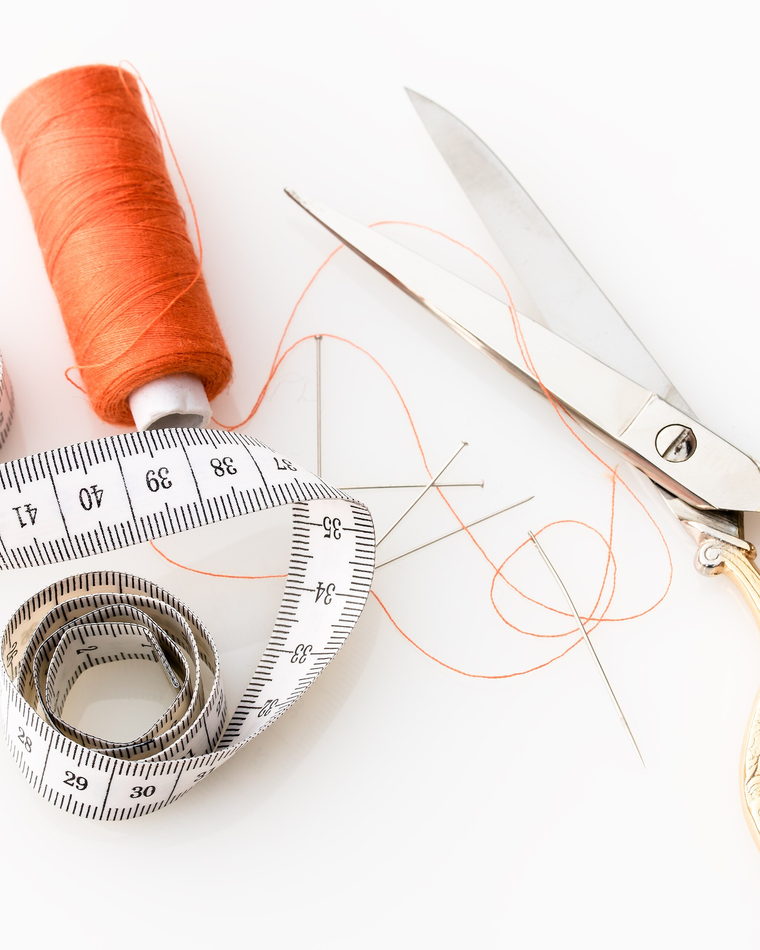 Dressmaking scissors, a tape measure and reels of thread arranged on a dark surface.