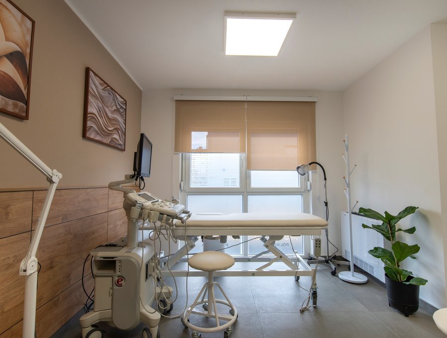 A consultation room with an examination couch, diagnostic console and daylight through the blinds