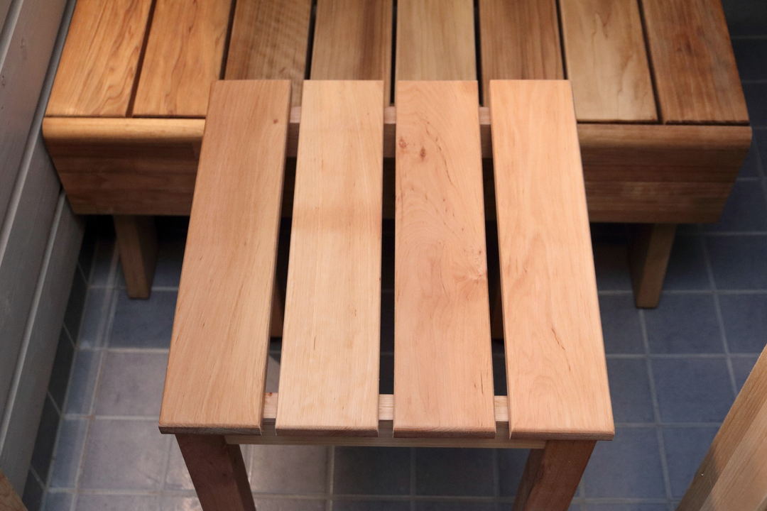 A light wooden slatted sauna stool standing on a darker wooden bench over blue tiles.