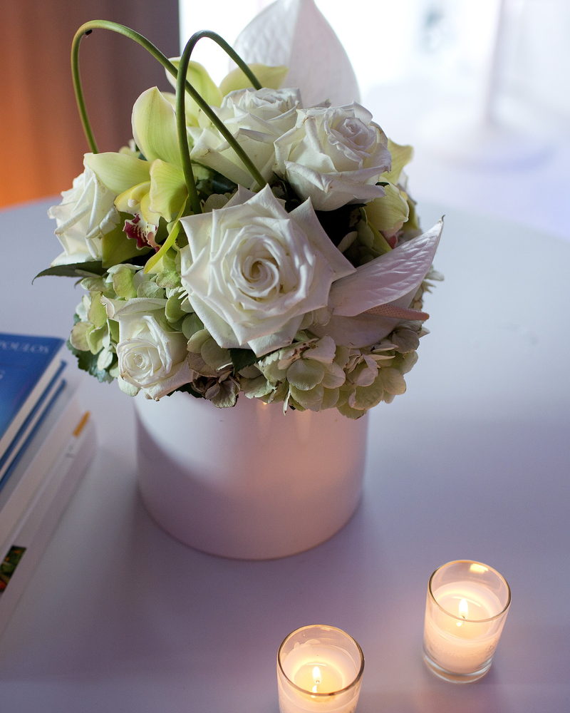 A white rose arrangement in a ceramic pot beside two lit candles on the front desk.