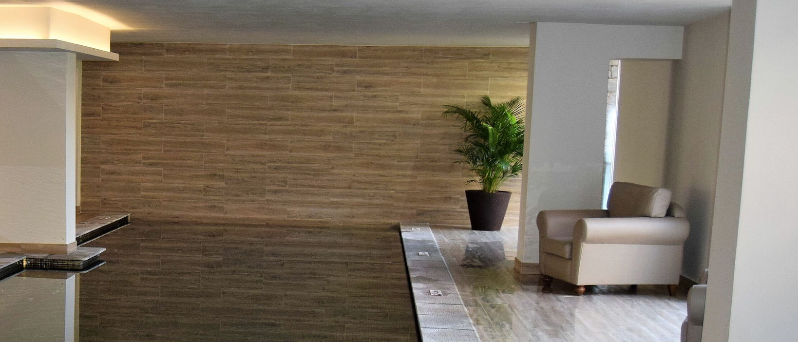 An indoor pool along a wood-effect wall, with a potted palm and a cream armchair.