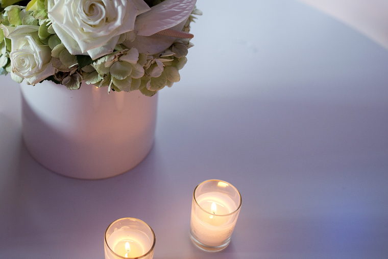 White roses in a vase and two lit candles on a low table.
