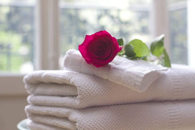 Folded white towels stacked with a single rose laid on top.