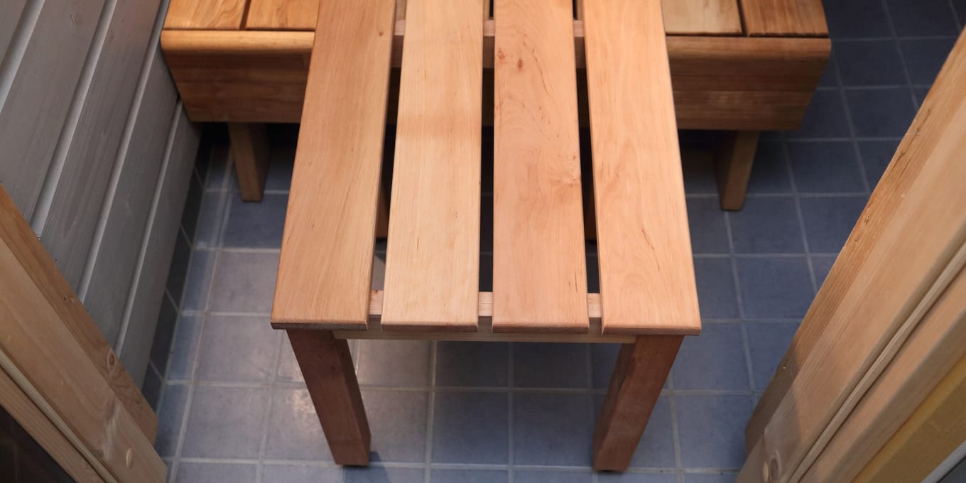 A plain wooden stool standing on a tiled sauna floor.