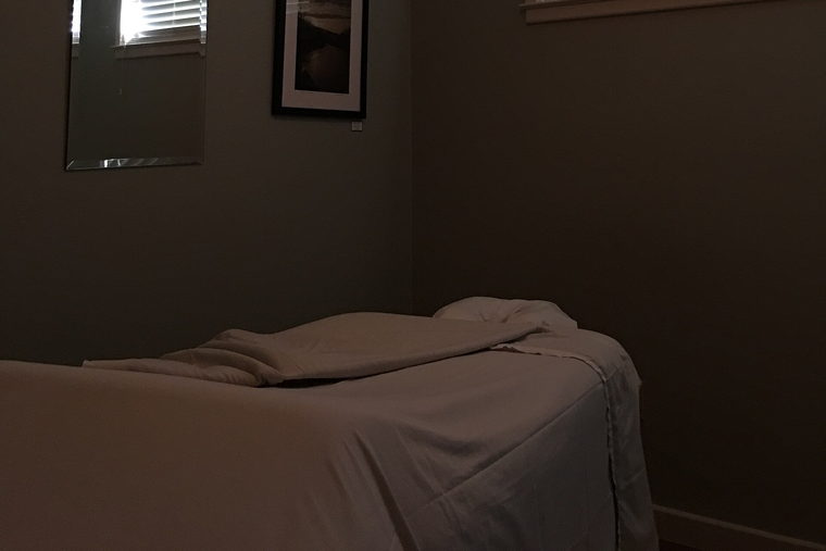 A dim treatment room with a massage table and a framed picture.