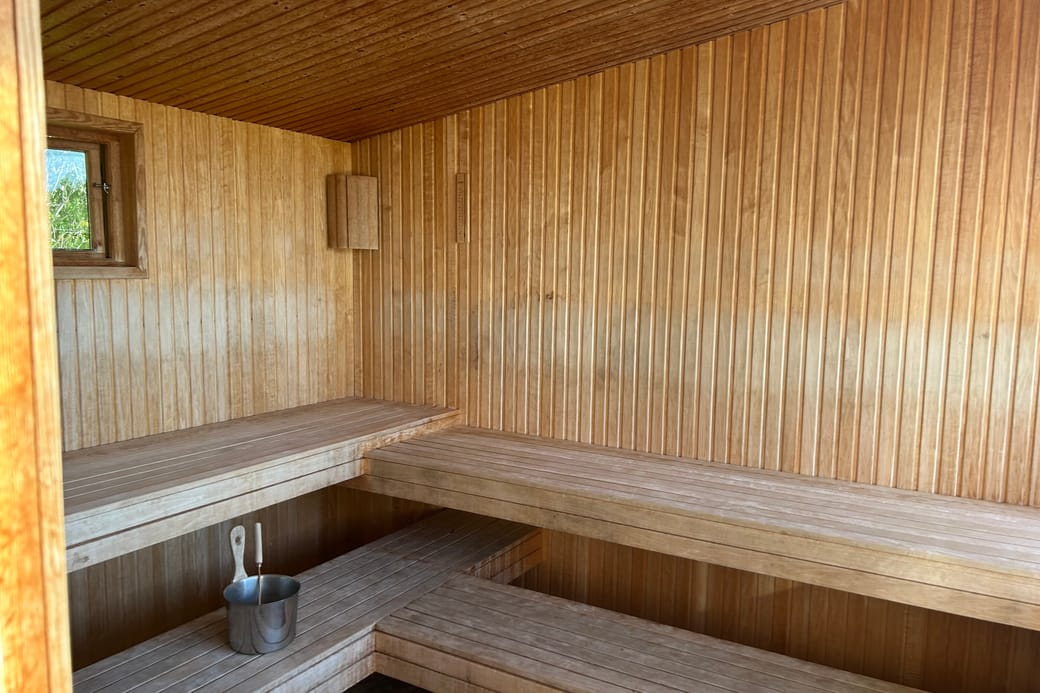 A timber-lined sauna with tiered benches, a small window and a wooden bucket on the floor.