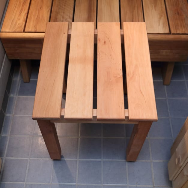 A slatted wooden stool on a tiled floor beside a longer bench.