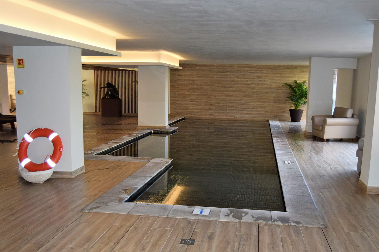 A quiet indoor pool set into a timber floor, with loungers and a plant at the far end.