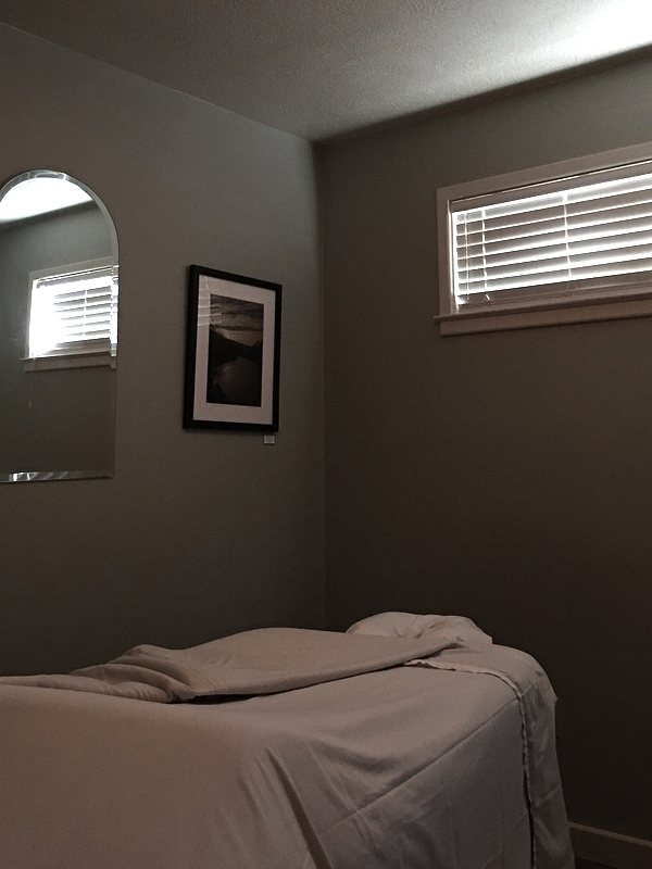 A quiet treatment room with a made-up table, a framed print and shuttered windows