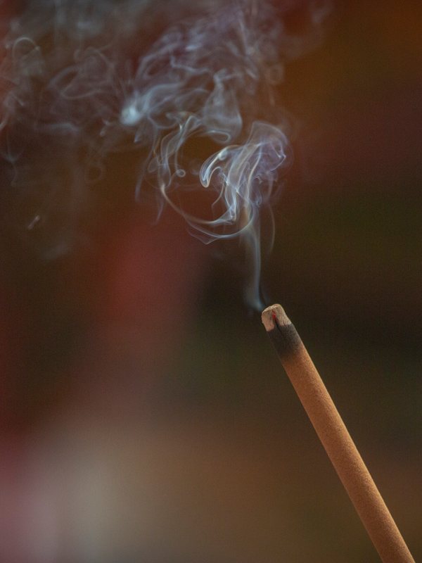 A single stick of incense burning, smoke curling in the dark
