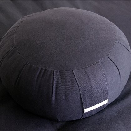 A round zafu meditation cushion in dark cotton resting on a folded cloth