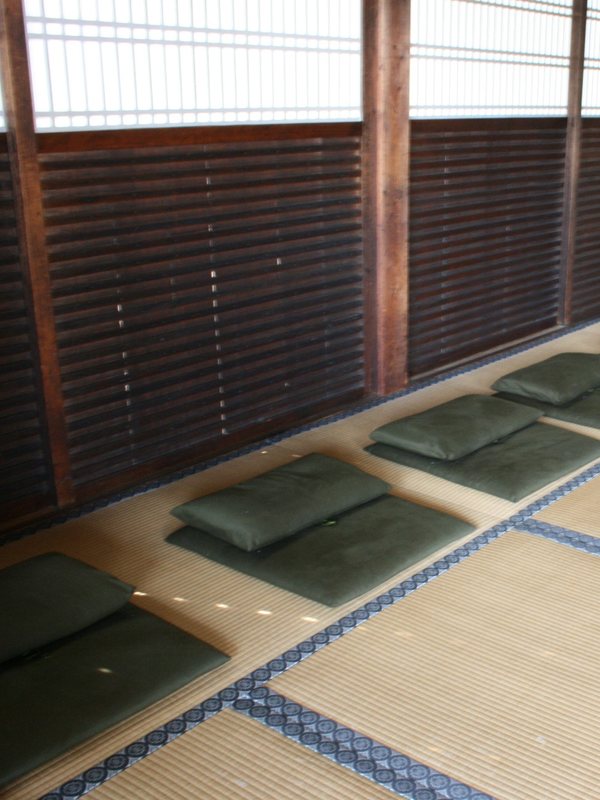 Flat cushions laid out on tatami matting beside a slatted wooden screen