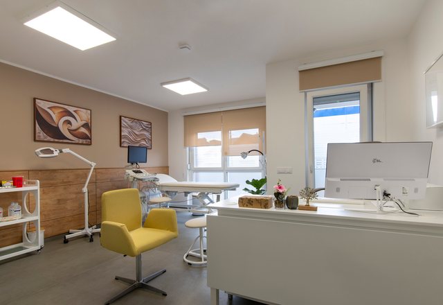 Treatment room with a yellow armchair, examination couch and a desk under framed prints