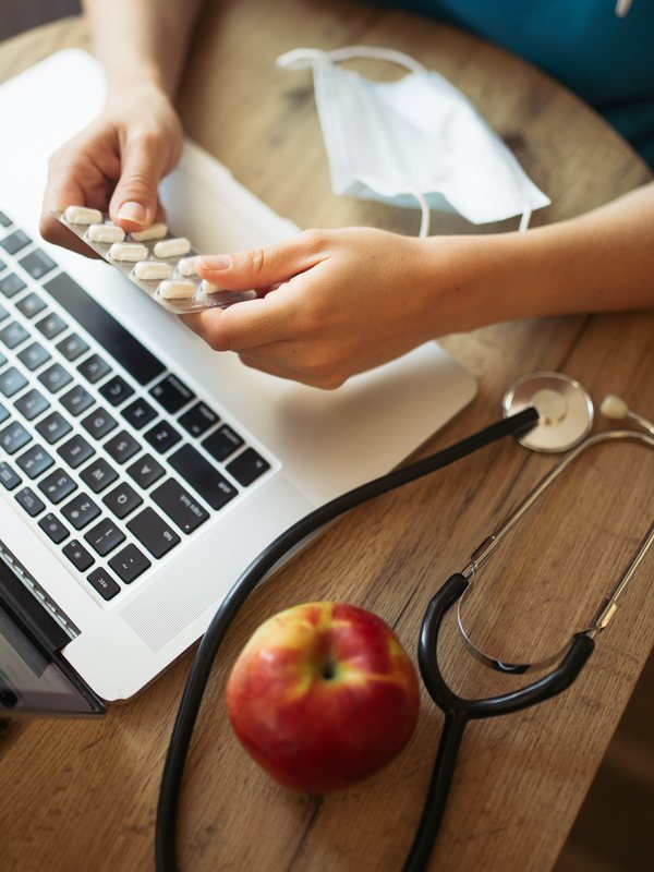 Tablets pressed from a blister pack beside a laptop, a stethoscope and an apple