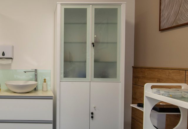 Glass-fronted supply cabinet, basin and instrument trolley in a treatment room