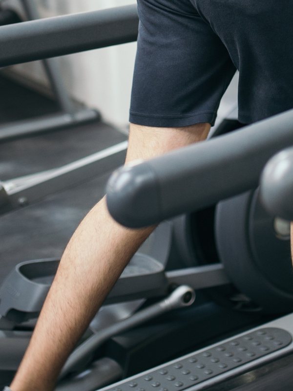 A member walking on a treadmill deck with one hand on the rail