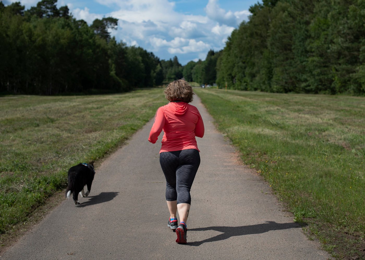A runner seen from behind on a paved country path with a black and white dog trotting alongside.