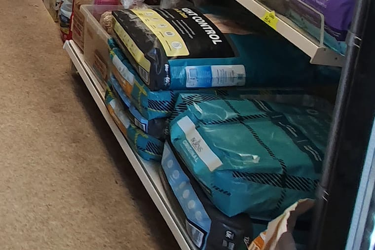 A shop shelf holding stacked bags of dog food, photographed from the aisle.