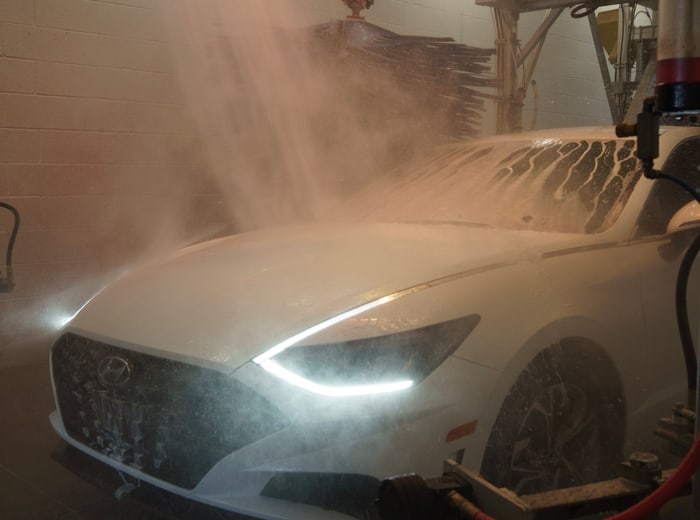 The same car rinsed clean under a cloud of spray, daytime running lights lit