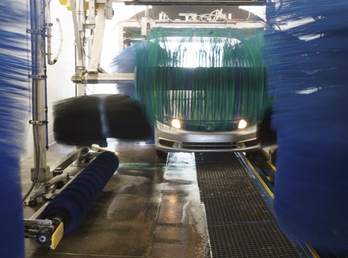 The wash rail with the green wrap-brush closing over a car's bonnet