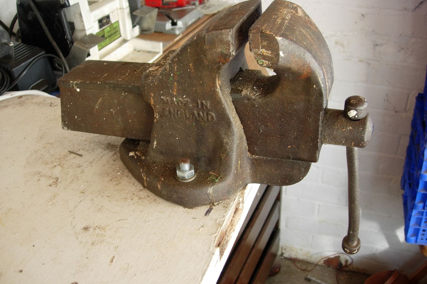 An old cast bench vice clamped to a workbench, its jaws open and its thread worn.