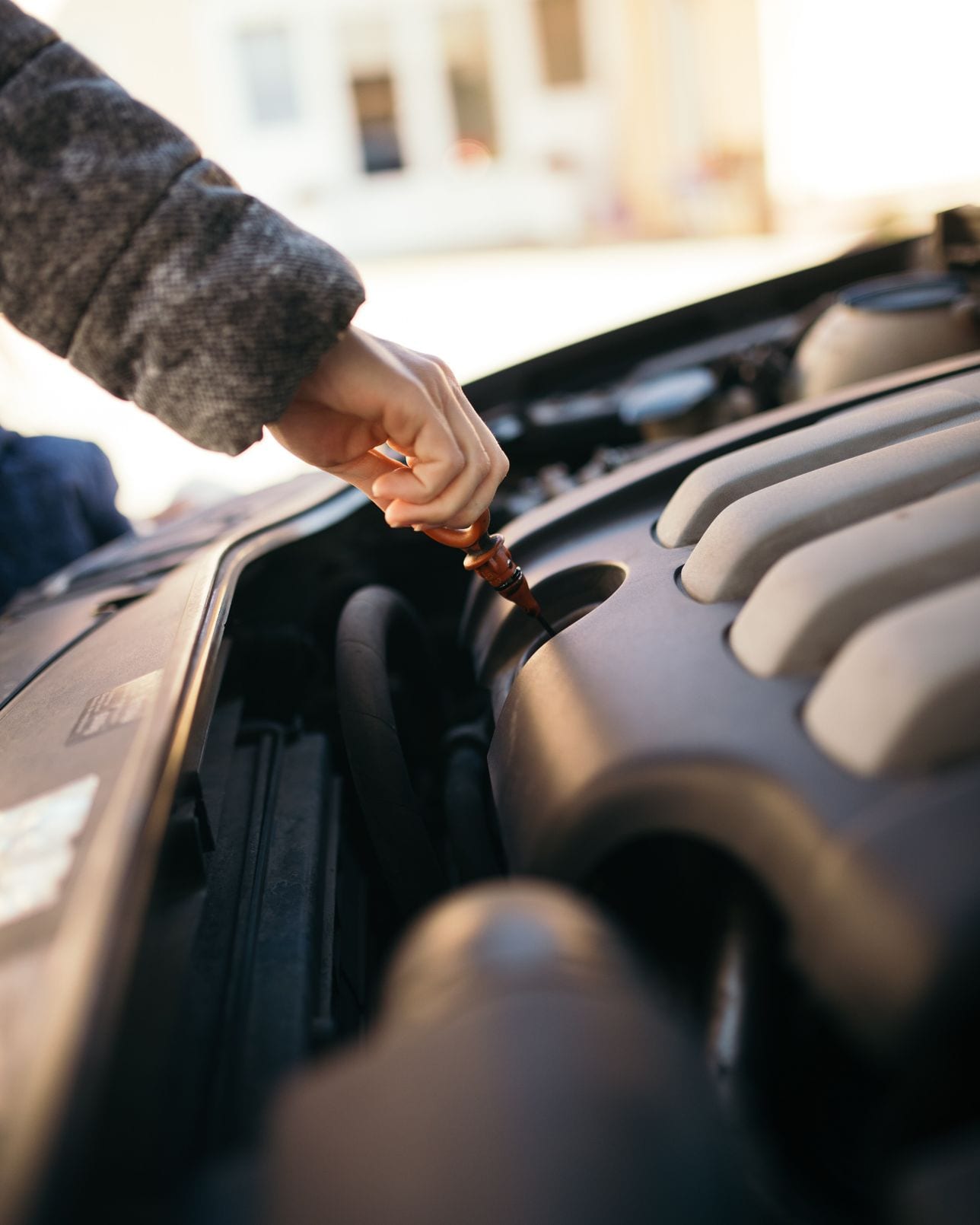 A hand drawing the dipstick to check the engine oil level under a raised hood.