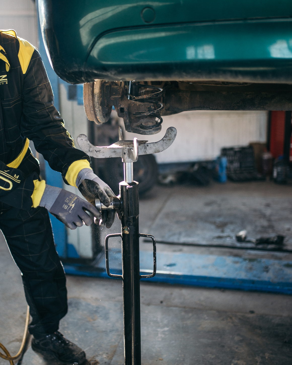 Hands at a suspension assembly on a vehicle raised over a workshop floor.